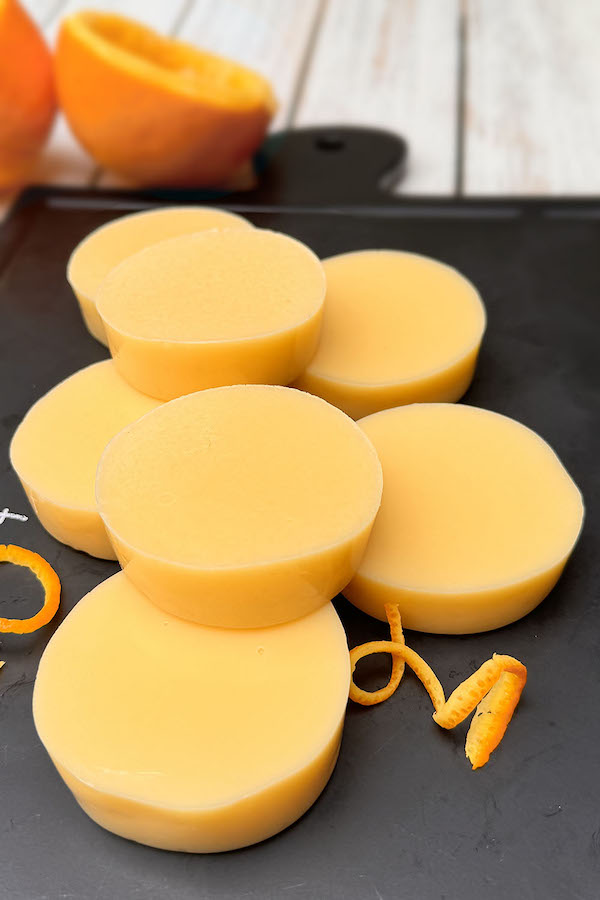Orange gummy snack bites on a serving board with orange curls and orange halves on the background.