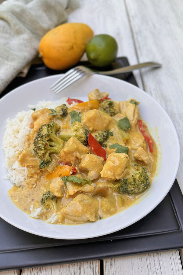 Mango chicken curry with thai-mex fusion in a bowl with yellow mango and lime in the background.