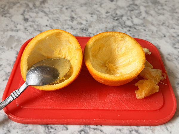 Emptied orange halves on a cutting board with a spoon.