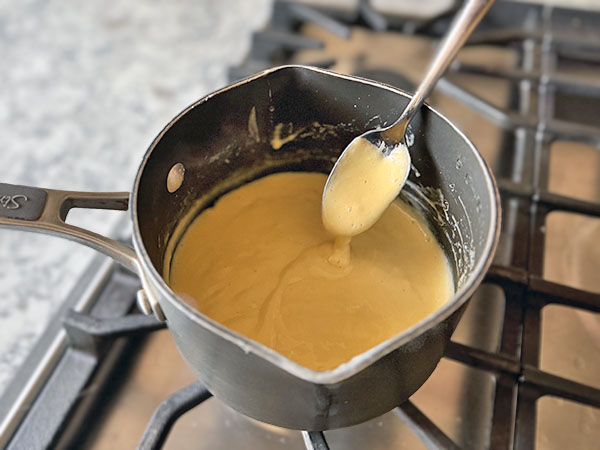 Thickened custard with a spoon in a saucepan on the stovetop.
