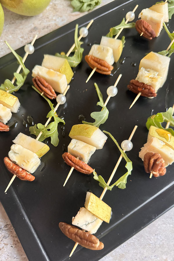 Pear and Blue Cheese Skewers with Arugula and Pecans drizzled with maple syrup on a serving board.
